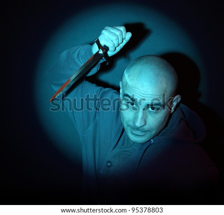 stock photo scary man with knife illuminated by a blue spotlight