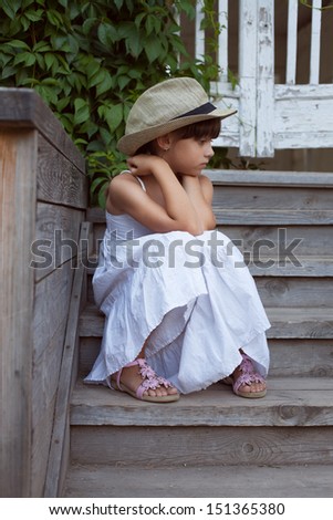 Sad little girl sitting alone on the porch