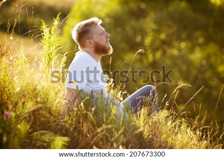Happy red-bearded man sitting on the grass and dreaming