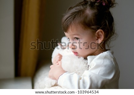 Portrait of little girl with teddy bear looking through a window