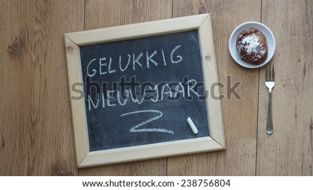 Happy new year in Dutch written on a chalkboard next to a Dutch donut