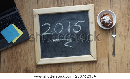 Happy 2015 written on a chalkboard next to a Dutch donut