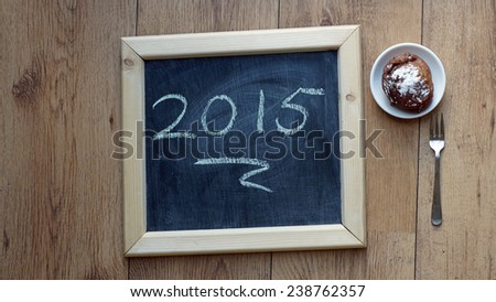 Happy 2015 written on a chalkboard next to a Dutch donut