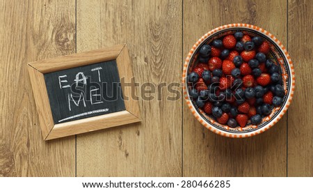 Eat me written on a chalkboard next to berries and strawberries