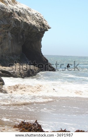A man in the ocean by a cliff and rocks in Santa Cruz, CA