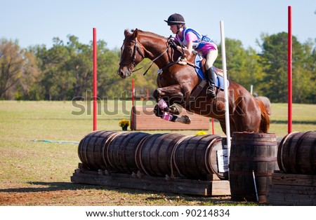 Young rider jumps over barrels on a cross country eventing course.