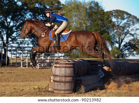 Teen rider leaps across a barrel jump on a cross country course