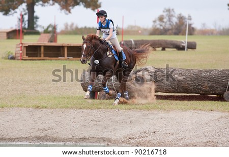 Young rider lands in a plume of dust after a jump over a log on a cross country course