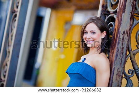Beautiful young woman with a blue necklace leaning against a metal pillar