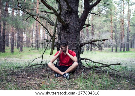 The young boy sits in fear under a tree