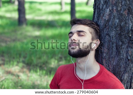 The boy sits under a tree and listens to music