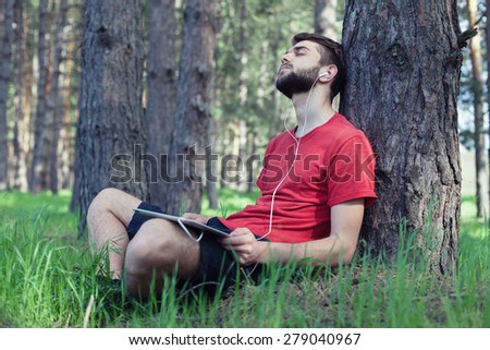 The boy sits under a tree and listens to music