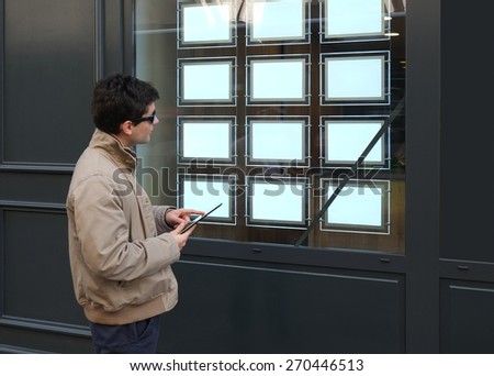 Make your choice! Man in front of a real estate office with empty brochure display. Focus on the white boards!