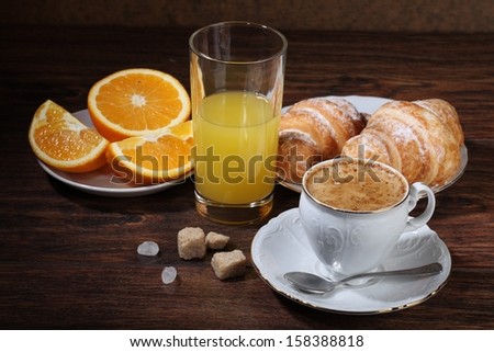 Fragrant fresh natural coffee with fresh orange juice and an appetizing croissant strewed by powdered sugar, a sweet juicy ripe orange