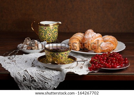 Fragrant tea in a beautiful cup and sweet appetizing tasty croissants from flaky pastry strewed by powdered sugar and berries of a ripe juicy sweet red currant