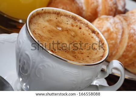 Fragrant tasty fresh black coffee with a tasty skin in a beautiful coffee cup and appetizing croissants from flaky pastry strewed by powdered sugar
