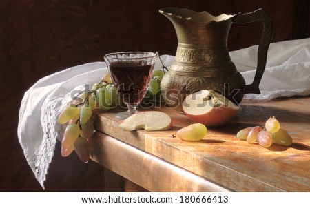 Still-life with a beautiful jug fresh fruit and red wine, a copper unusual jug and clusters of juicy pink grapes both sweet fragrant apples and red wine in a beautiful crystal wine-glass
