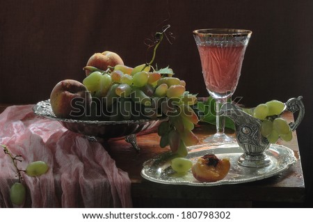 Still-life with pink wine in a crystal glass and fresh fruit, fresh appetizing juicy peaches and clusters of ripe grapes in a vase for fruit and invigorating pink wine in a wine glass on a long leg