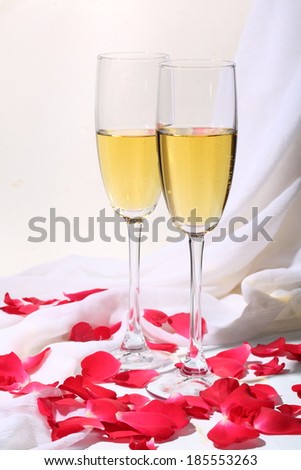 Still-life with beautiful wine glasses and petals of roses, graceful glasses filled with champagne on a table covered with petals of red roses