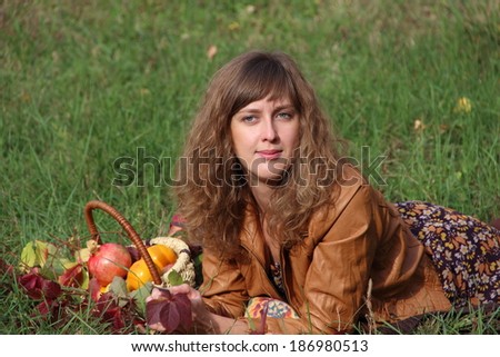The beautiful young girl with red hair and green eyes with a bright autumn bouquet and fresh fruit in a wattled basket