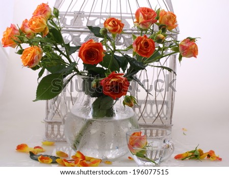 Still-life with a transparent cup and a beautiful bouquet from bright orange roses in a transparent jug