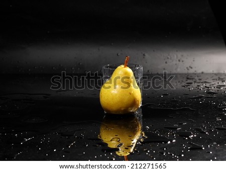 Dynamics of a liquid, juicy sweet appetizing pear in a glass with splashed out water on a dark surface of a table