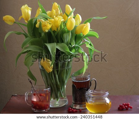 Still-life with tea, honey in transparent bank, a guelder-rose and a bouquet of yellow tulips