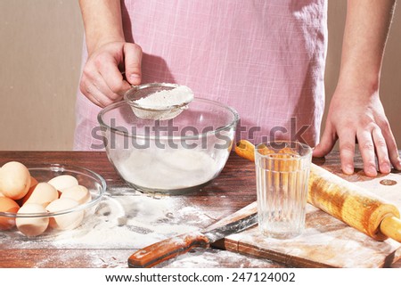 The man\'s hand sifts a flour in a cup through a sieve
