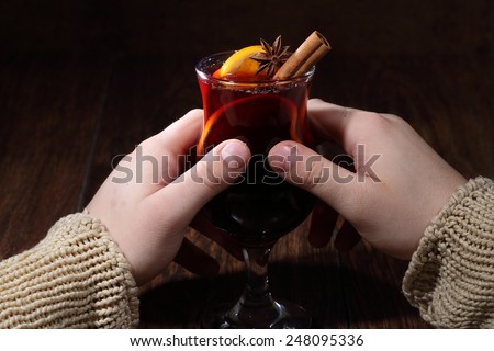 Man\'s hands hold a glass with mulled wine, mulled wine with an orange, honey, cinnamon, a carnation and an anise