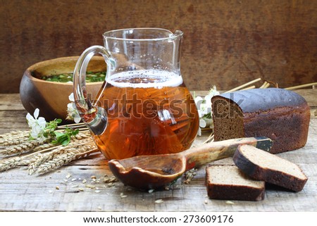 Jug with kvass, okroshka and rye bread on a wooden table