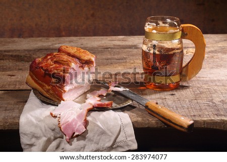 Beer with foam in a transparent mug and smoked meat with a fat layer