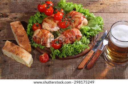 Beer in a transparent mug and chicken beaters in bacon submitted with greens, bread and tomatoes