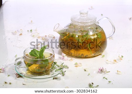 Tea from grasses and mint in a transparent teapot and a cup on a white background