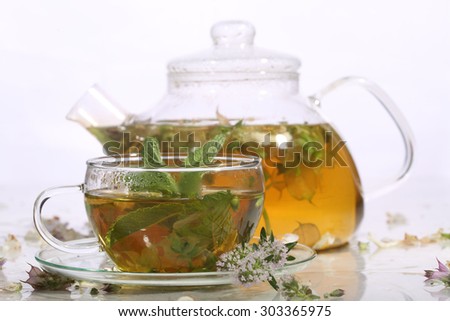 Tea from grasses and mint in a transparent teapot and a cup on a white background