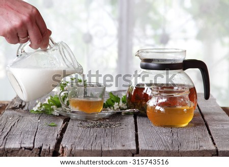 The man\'s hand holds a transparent jug with milk over a cup of tea