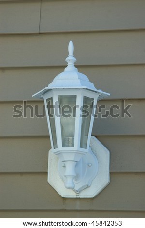 A white porch light against a brown vinal siding
