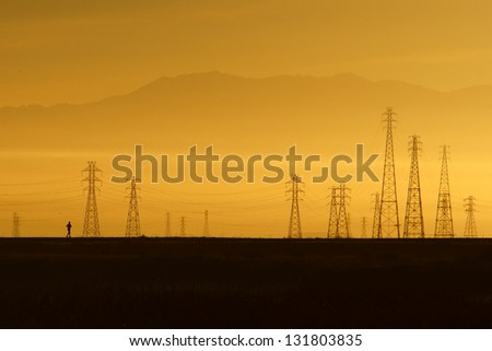 A morning runner runs through a nature preserve in San Francisco Bay Area, California, USA. The power transmission towers and distant mountains formed an impressive backdrop against the morning light.
