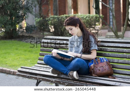 Student sitting on old wood bench and reading blue book, outdoor.