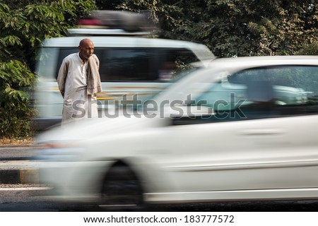 UTTAR PRADESH, INDIA - NOVEMBER 15, 2012: Unidentified Indian man crosses the street with moving cars (motion blurred). The frequency of traffic accidents in India is amongst the highest in the world