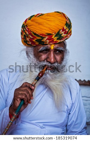 JODHPUR, INDIA - NOVEMBER 26, 2012: Old Indian man smokes hookah (waterpipe) in Mehrangarh fort. The concept of hookah is thought to have originated In India