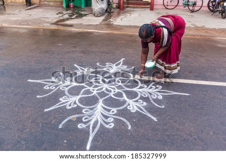 TIRUCHIRAPPALLI, INDIA - FEBRUARY 14, 2013: Unidentified India woman drawing Kolam (Rangoli) - form of painting drawn by using rice powder in front of the house - thought to bring prosperity to homes