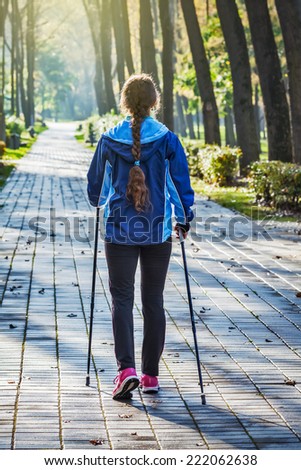 Nordic walking adventure and exercising concept - woman hiking withnordic walking poles in autumn park