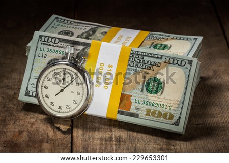 Time is money loan concept background - stopwatch and stack of new 100 US dollars 2013 edition banknotes (bills) bundles on wooden background