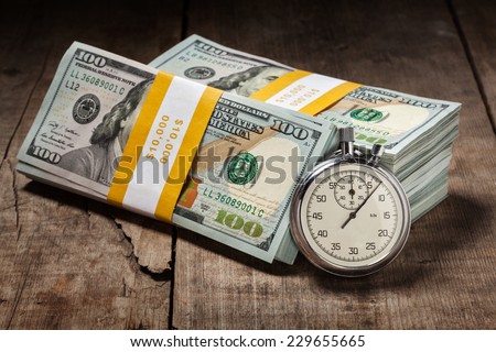 Time is money loan debt deadline concept background - stopwatch and stack of new 100 US dollars 2013 edition banknotes (bills) bundles on wooden background