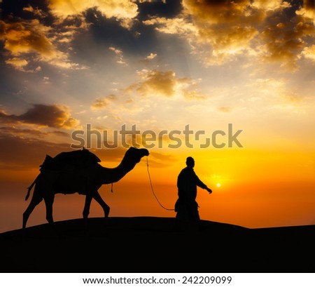 Rajasthan travel background - indian cameleer (camel driver) with camel silhouette in dunes of Thar desert on sunset. Jaisalmer, Rajasthan, India