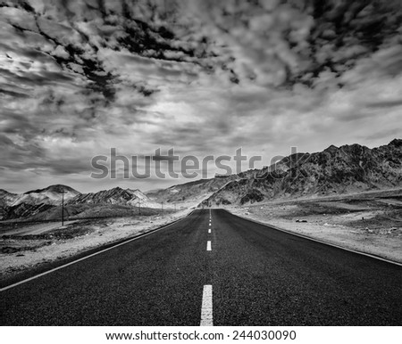 Travel forward concept background - road in Himalayas with mountains and dramatic clouds. Ladakh, Jammu and Kashmir, India. Black and white version