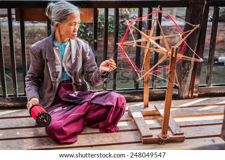 INLE LAKE, MYANMAR - JANUARY 8, 2014: Burmese woman wheel spinning yarn at weaving factory where textile is manufactured in traditional way