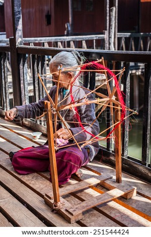 INLE LAKE, MYANMAR - JANUARY 8, 2014: Burmese woman wheel spinning yarn at weaving factory where textile is manufactured in traditional way