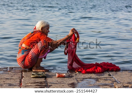 MAHESHWAR, INDIA - APRIL 26, 2011: Old Indian woman washing sari on sacred river Narmada ghats. To Hindus Narmada is one of 5 holy rivers of India