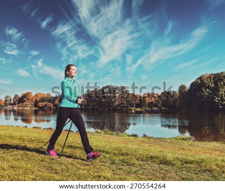Vintage retro effect filtered hipster style image of nordic walking adventure and exercising - young woman hiking with nordic walking poles in park along river